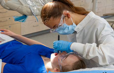 two dental students practice using tools in an educational setting. one is acting as the student while the other practices.